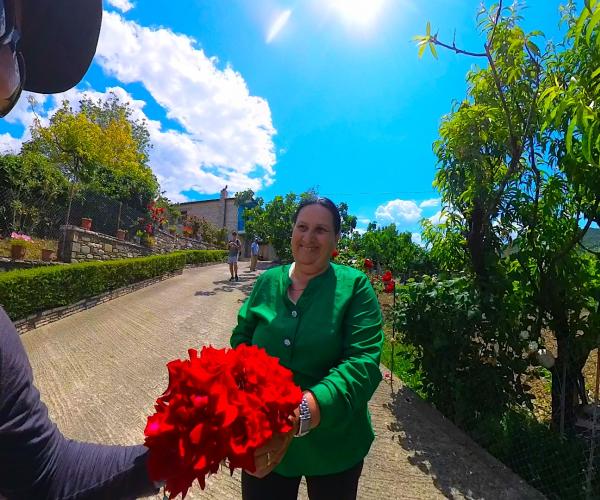 Local woman offering red flowers during a farm visit near Roshnik.